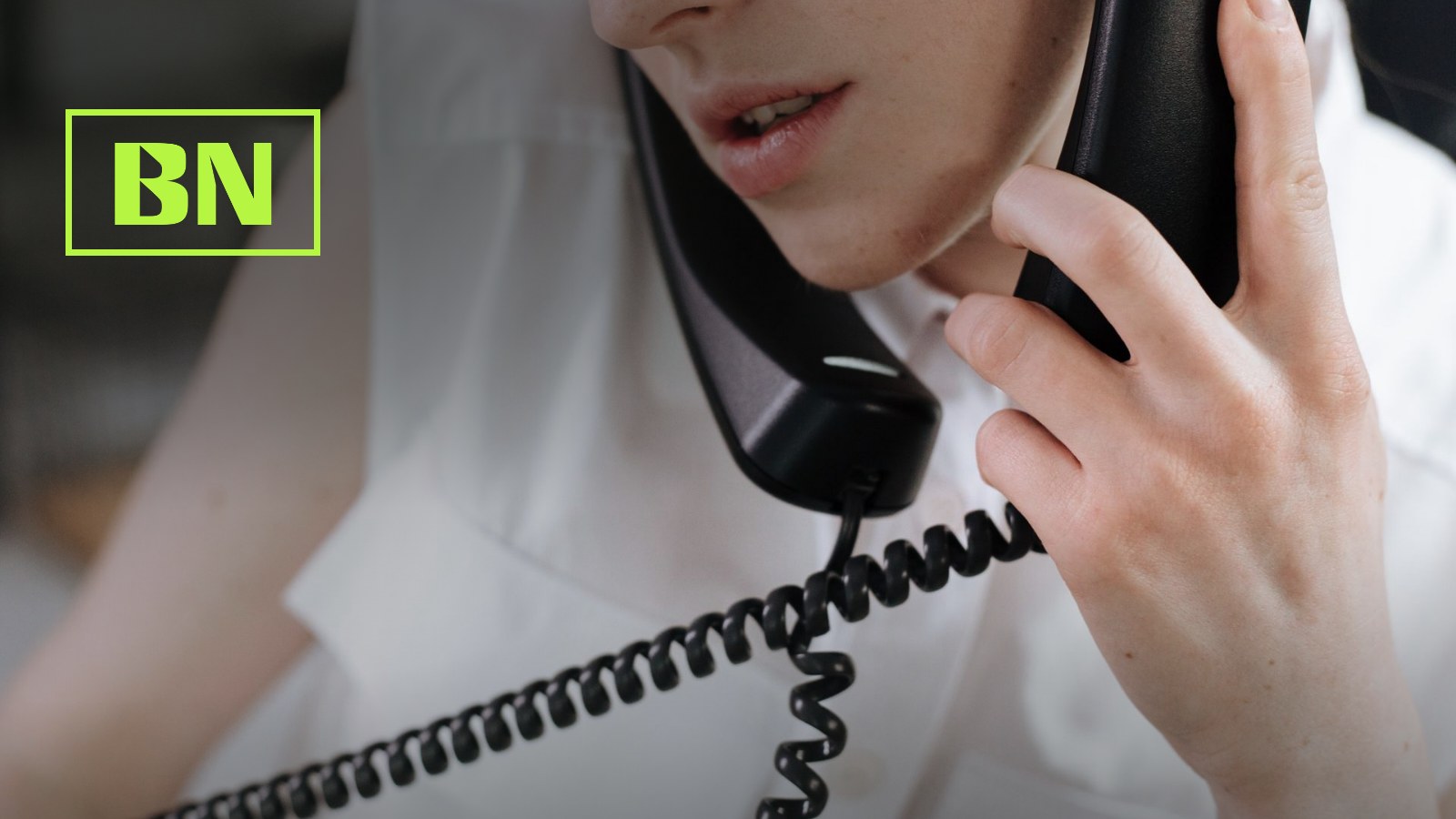 Nahaufnahme einer Person, die einen schwarzen Telefonhoerer ans Ohr haelt und spricht